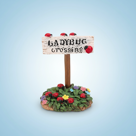 Ladybug Crossing miniature fairy garden sign with red ladybugs and colourful flowers on a light blue background